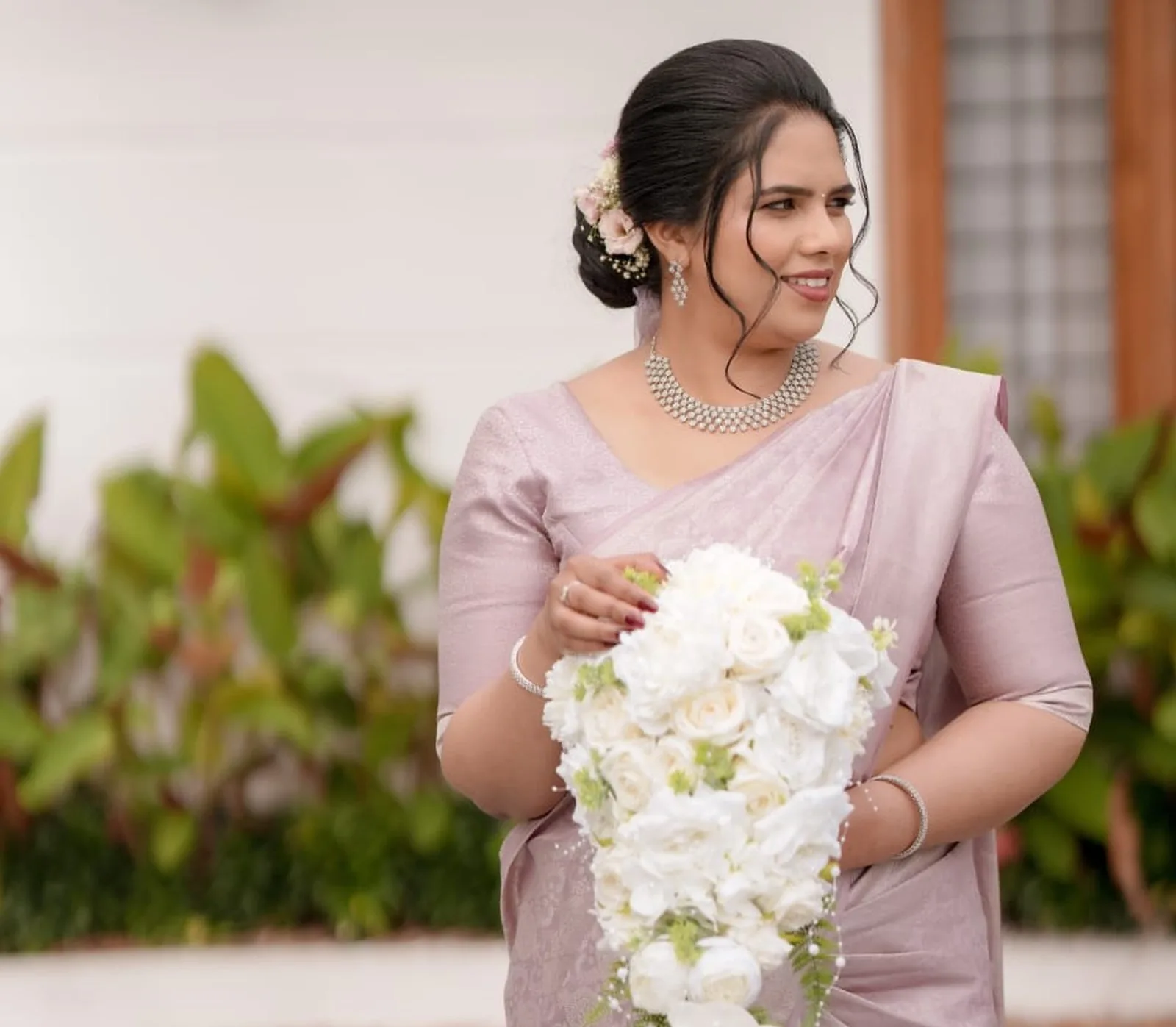 Real bride in a blush pink saree holding a white bouquet — soft glam bridal makeup by Ammu Bridal Studio